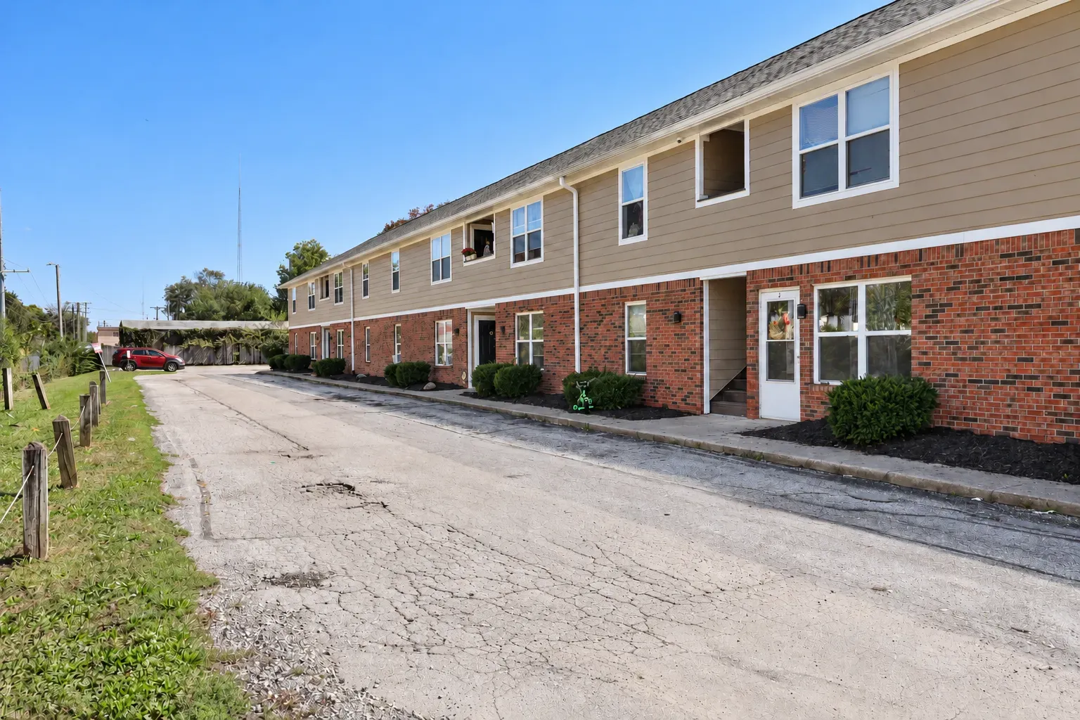 Front of Center Place Apartments, Greenfield: brick lower story, tan siding, shrubs and unit entries along the drive