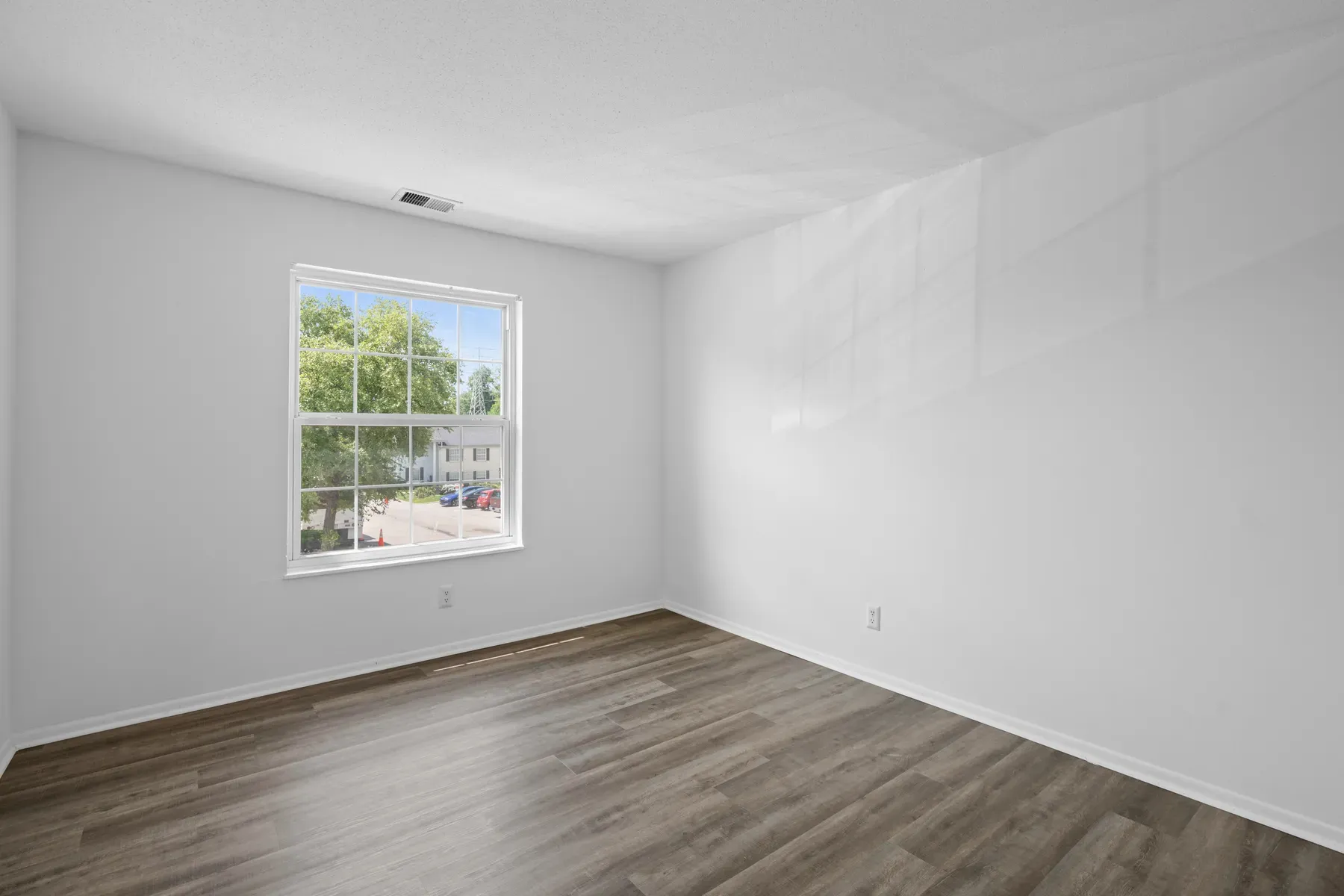 Empty bedroom with a double-hung window, white walls and wood-look flooring
