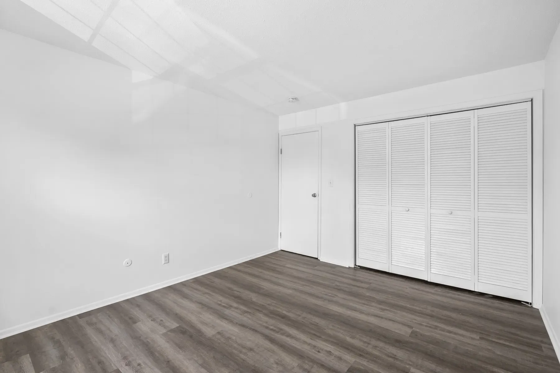 Bedroom with louvered closet doors and wood-look flooring