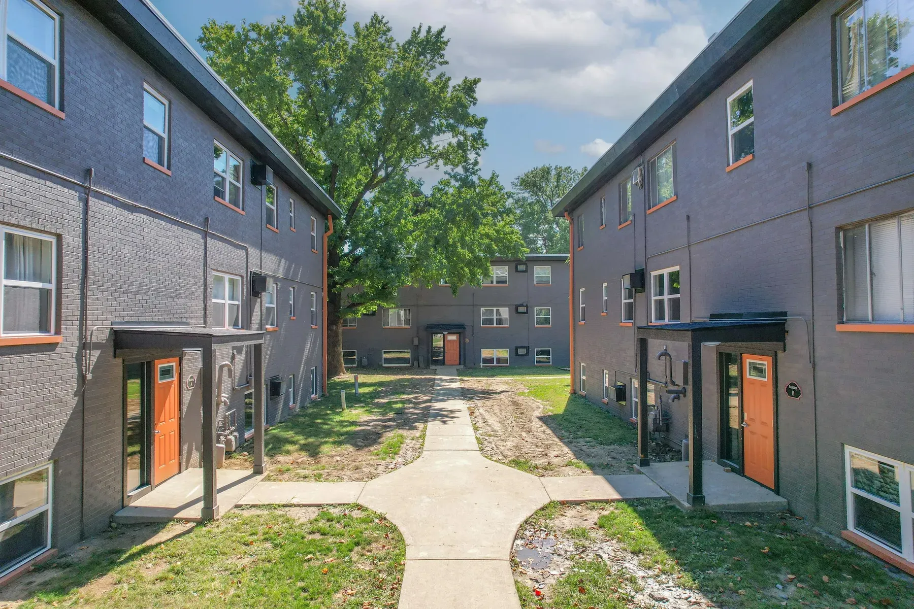 Brick apartment buildings with orange entry doors along a courtyard walkway