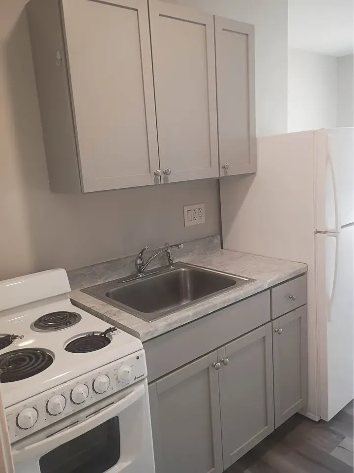 Studio kitchen with gray shaker cabinets, a stainless sink, white range and refrigerator at New Palestine Apartments, New Palestine