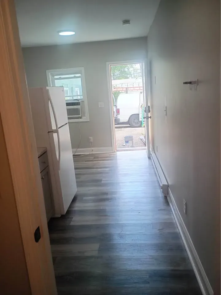 Studio hallway with wood-look flooring past the refrigerator to an open door at New Palestine Apartments, New Palestine