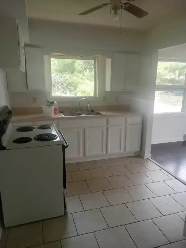 Three-bedroom kitchen with white cabinets, an electric range, tile floor and two windows at New Palestine Apartments, New Palestine