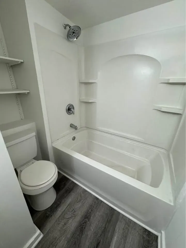 Bathroom with a white tub-shower surround and wood-look flooring at New Palestine Apartments, New Palestine