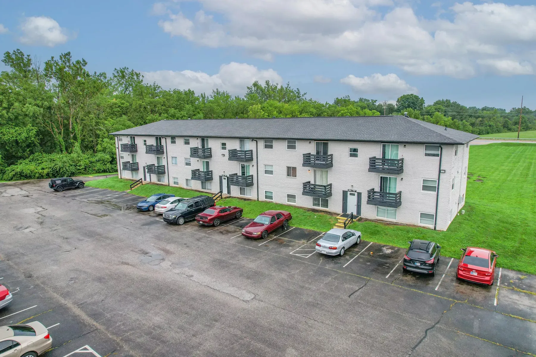 Elevated view of the three-story white brick building with dark balconies, a front lawn and the parking lot