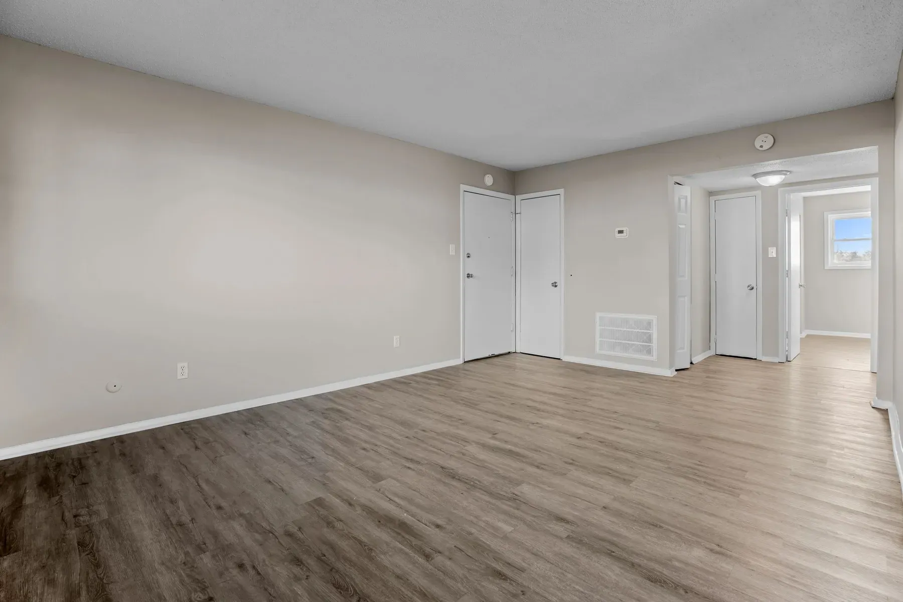 Living area with neutral walls, wood-look flooring and a hallway