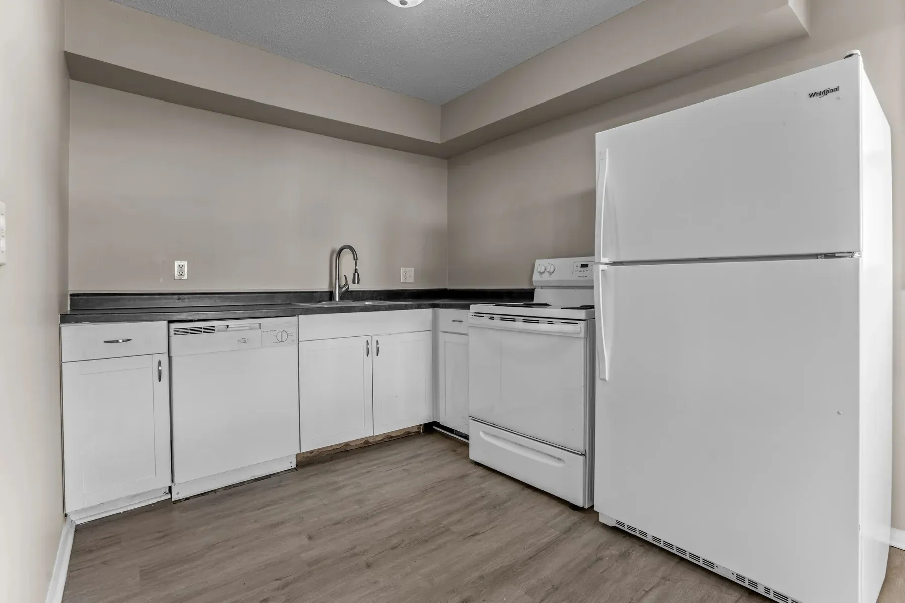 Kitchen with white cabinets, dark counters, a dishwasher and refrigerator